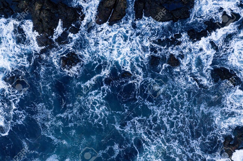 Aerial view of ocean waves breaking over dark coastal rocks